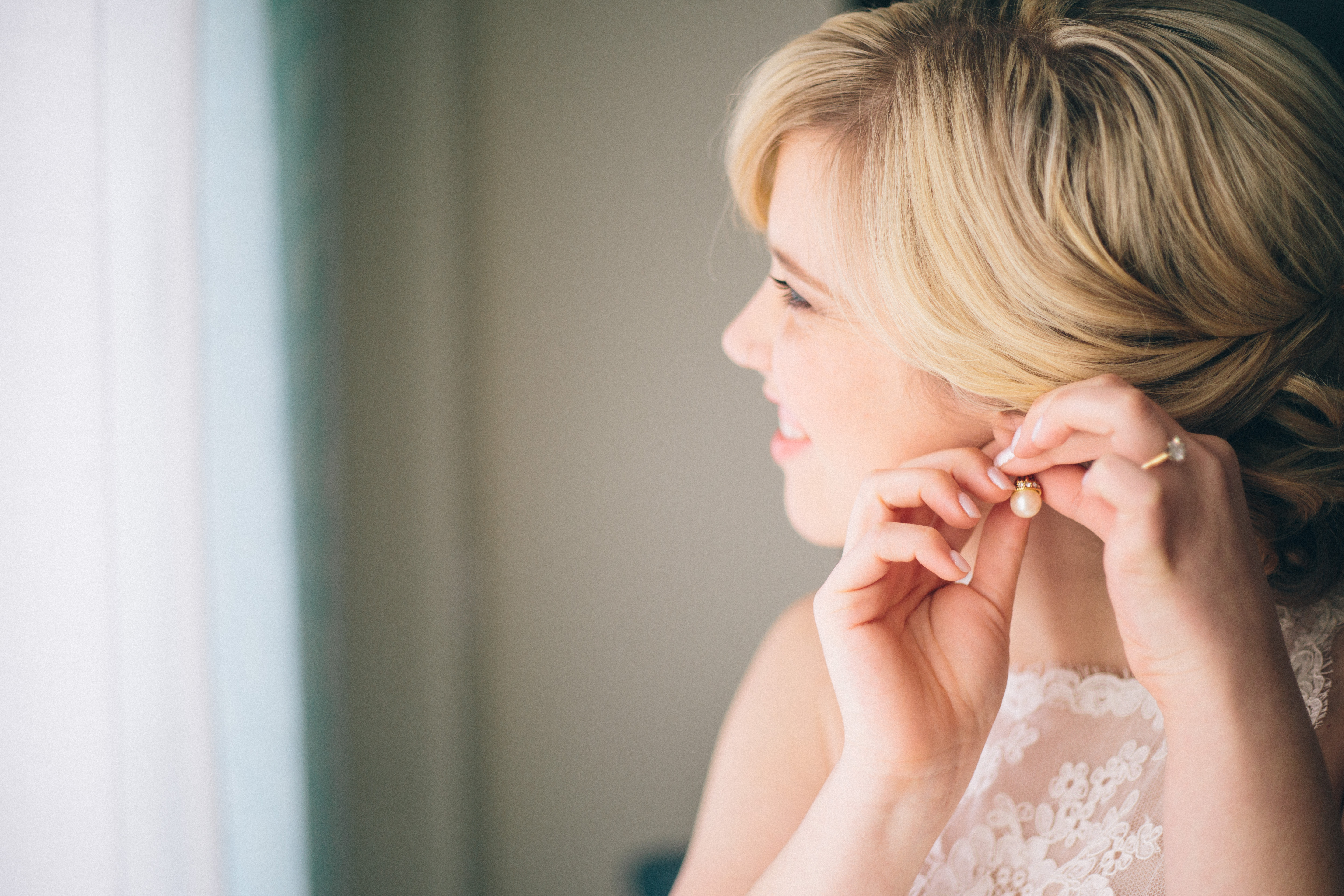 Blonde bride with classic low bun up-do puts on her pearl earring before her Christmas winter wedding in Toronto