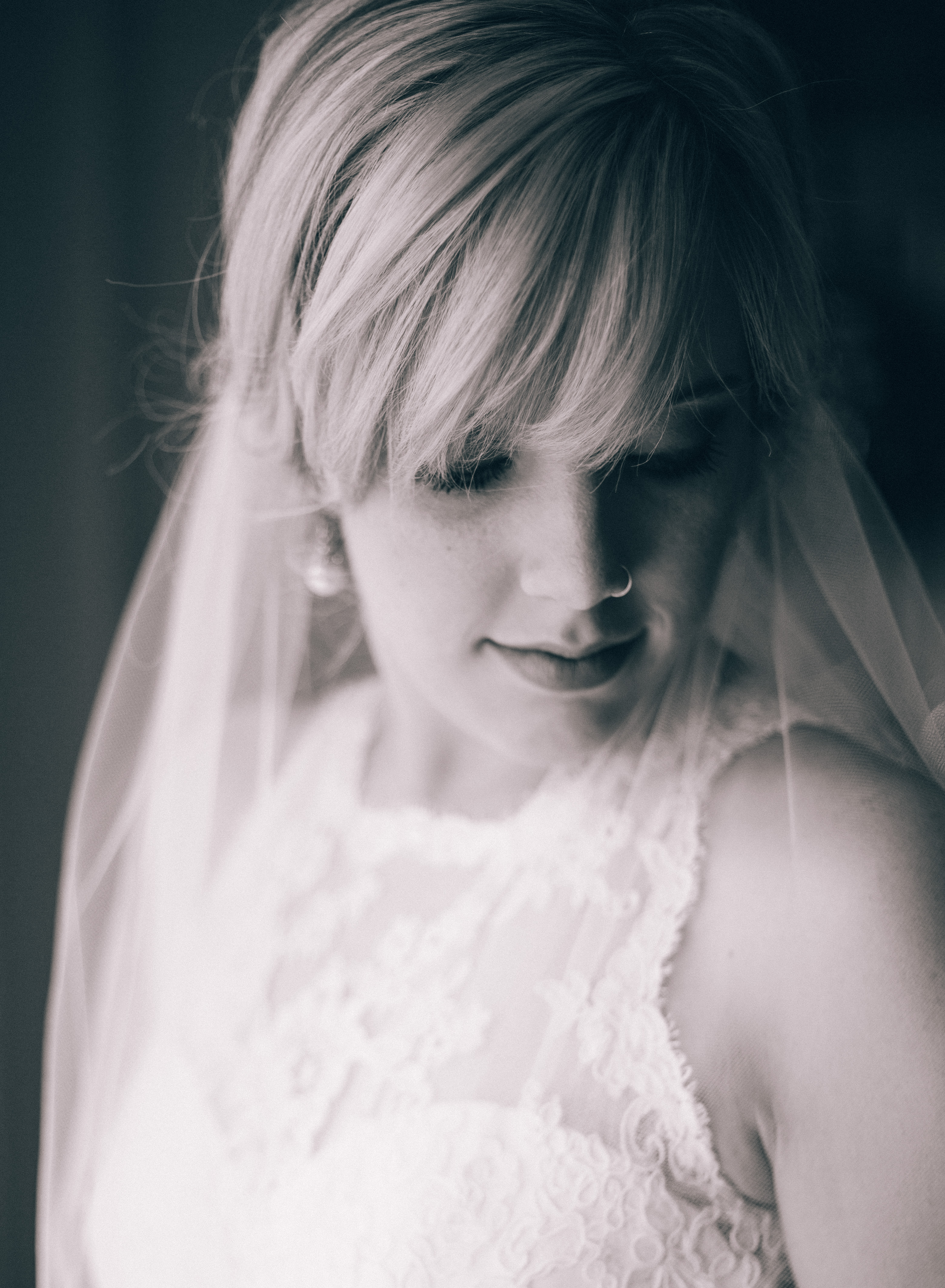 Black and white image of blonde bride with long bangs and classic hairstyle wearing pearl earrings and low set veil