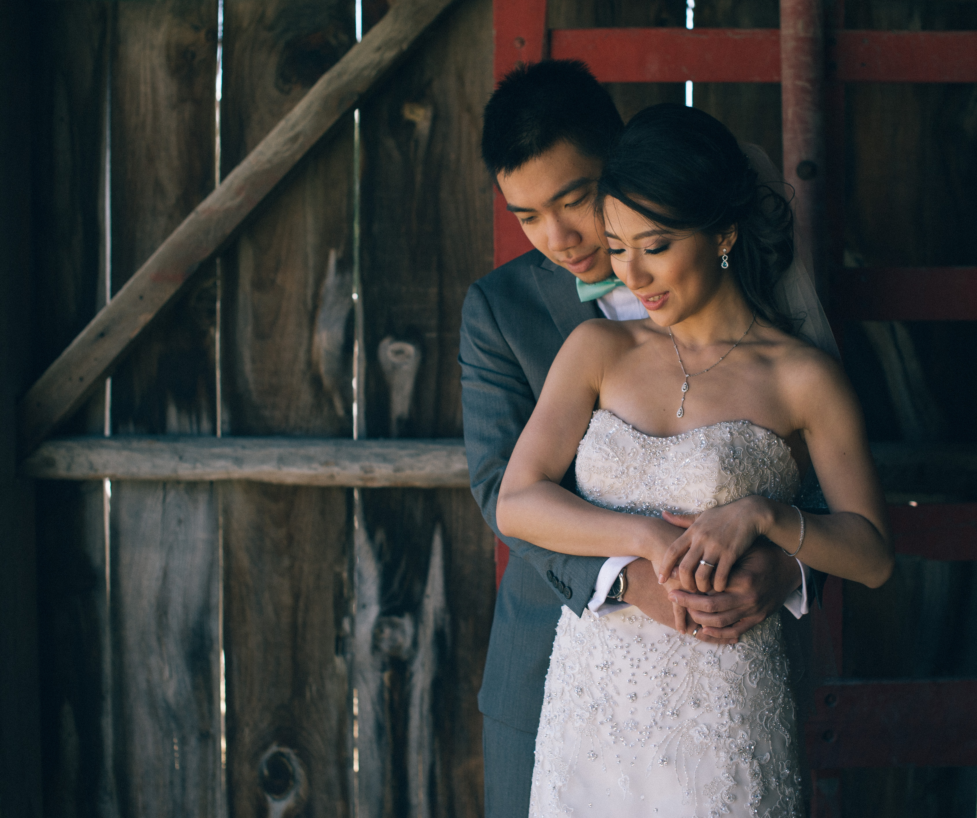 Chinese groom holding bride wearing a beaded sweetheart wedding dress inside large shed at Markham Museum