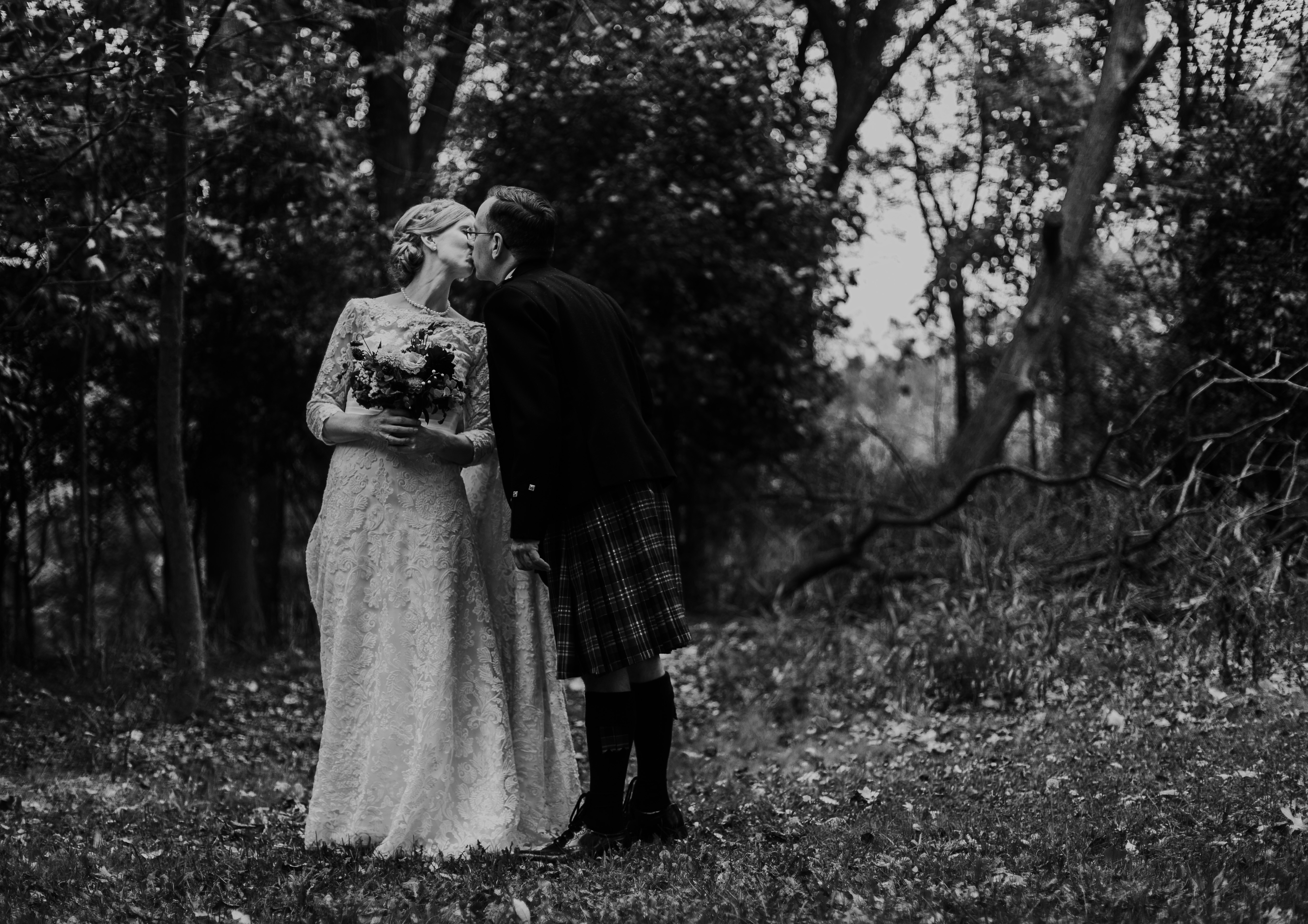 Bride wearing long sleeve lace wedding gown leans over to share a kiss with groom wearing Scottish kilt at their fall Christian wedding